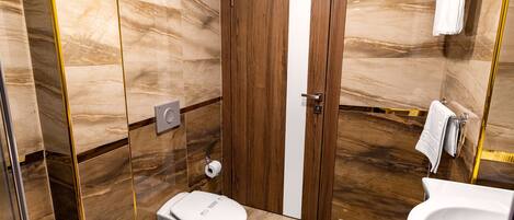A modern bathroom with a marble floor, a wooden door, a toilet, a sink, and a towel rack.