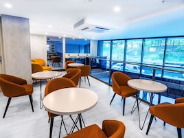 A modern interior with round tables and orange chairs, large windows offering a view of the outside.