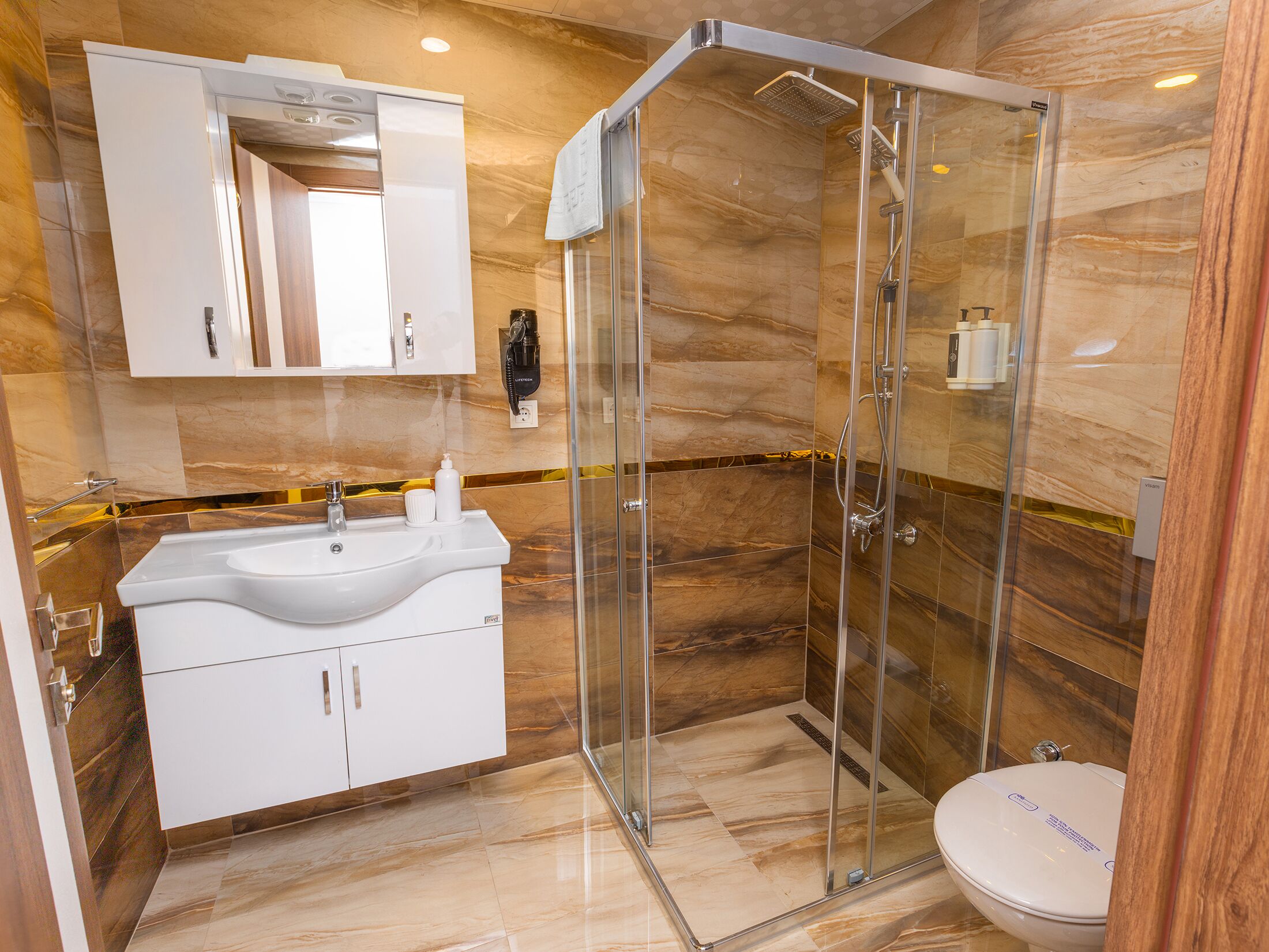Un baño moderno con ducha envuelta en vidrio, un lavamanos blanco con encimera de mármol y un espejo grande encima.