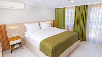 Une chambre d’hôtel moderne dotée d’un grand lit, d’une table de chevet, d’un climatiseur intégré et d’une fenêtre avec des rideaux légers.