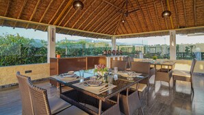 Un espace extérieur aménagé pour les repas, avec des meubles en osier, une table en verre et un toit de chaume.