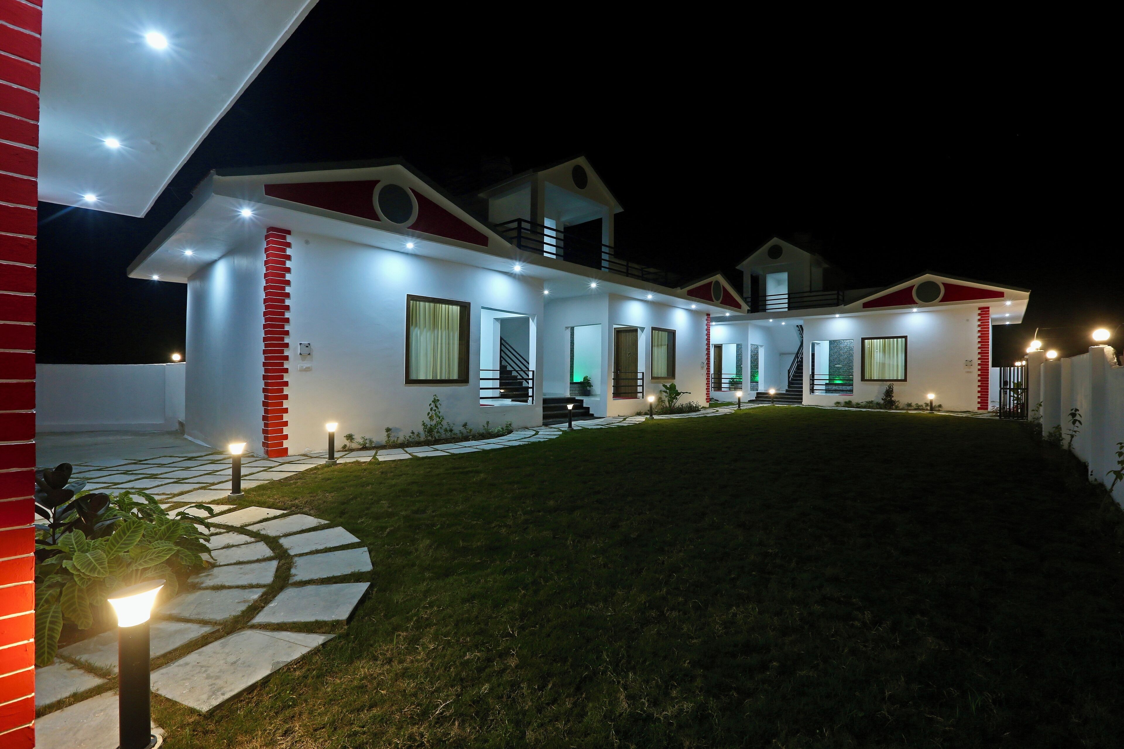 A modern two-story house with a well-lit exterior, a visible staircase, and a paved driveway.