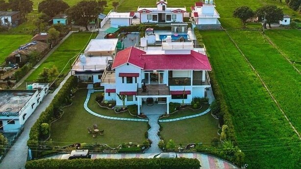Un grand bâtiment à plusieurs étages, doté d’un toit rouge, entouré de champs verdoyants et traversé par une rivière.