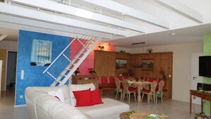 A spacious living area with a white sofa, red cushions, a wooden dining table with chairs, and a staircase with a metal railing. - Hof Eckhorst - View apartment - Stylish ambience & cozy atmosphere (Güby)