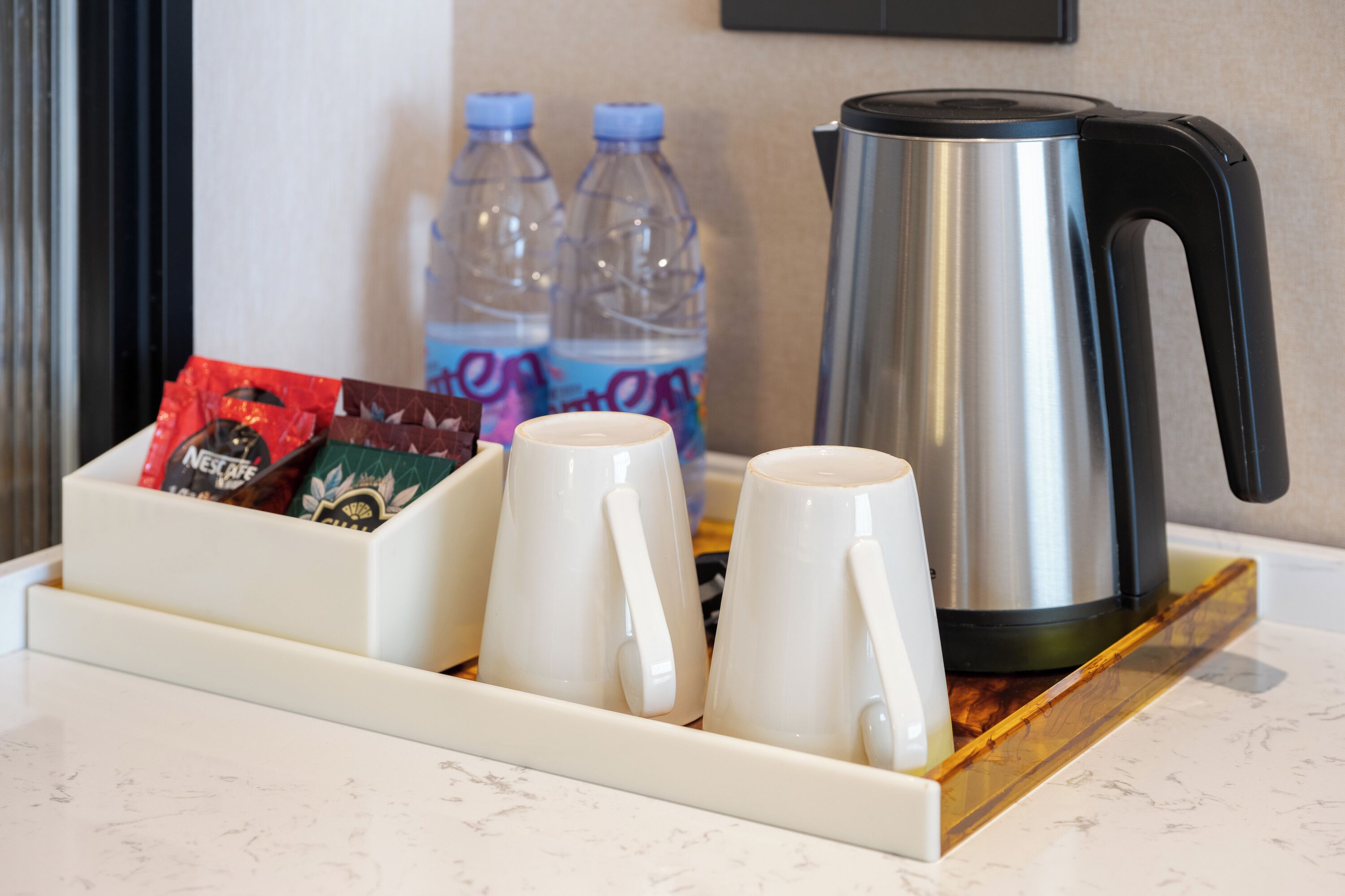Een dienblad met twee witte mokken, een roestvrijstalen koffiepot en twee waterflessen op een marmeren aanrecht.