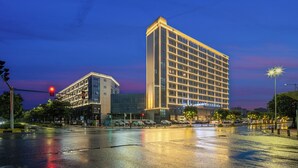 A modern hotel with a prominent corner building, a wet street reflecting lights, and a traffic light. - Rezen Longuu Hotel - Guangzhou Baiyun Airport Cultural Tourism City (Guangzhou)