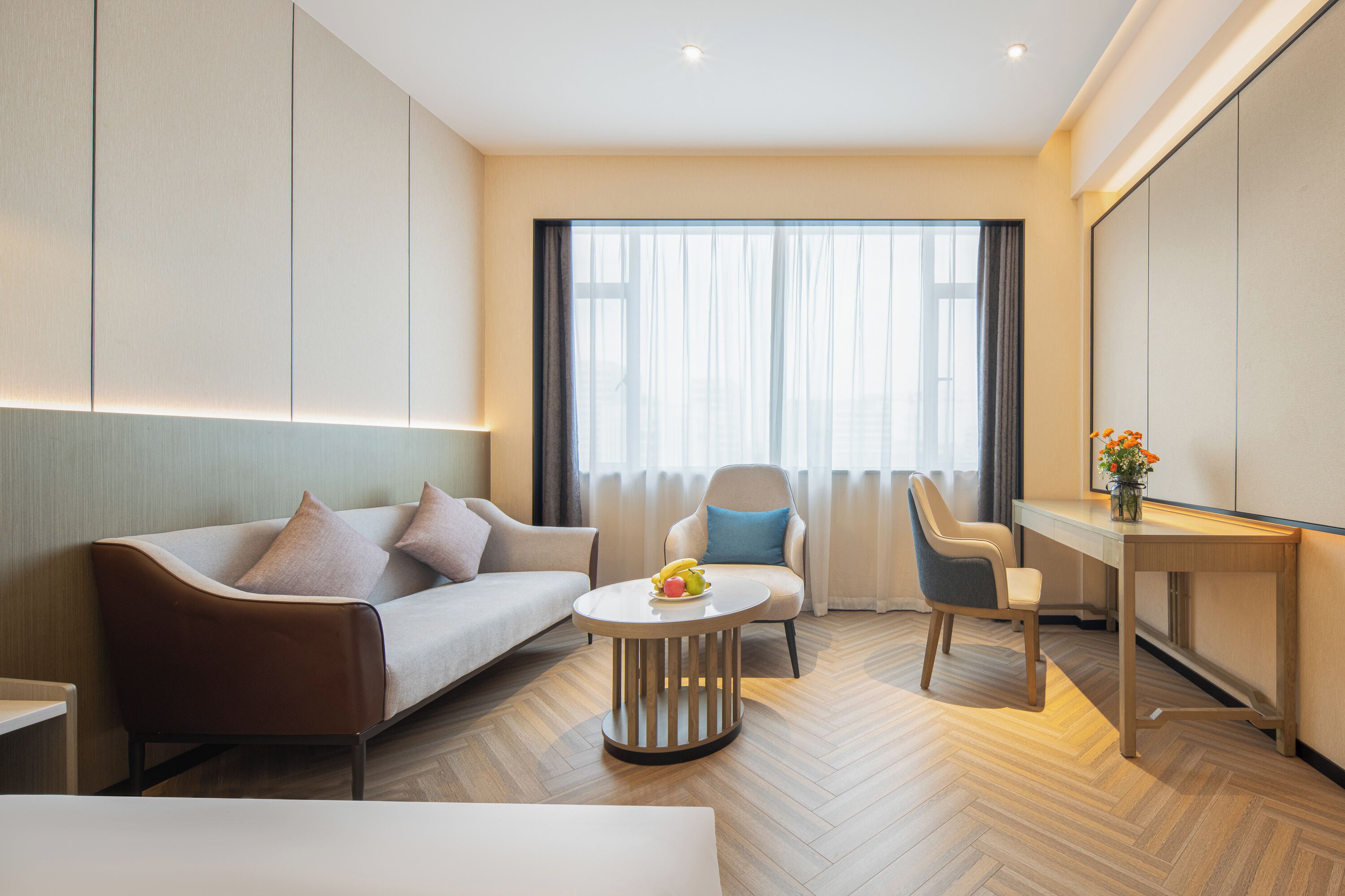 Una habitación de hotel moderna con sofá, una silla, una mesita redonda y un escritorio.
