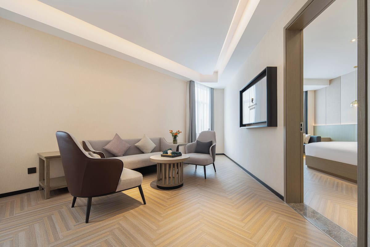 A modern hotel room with a sofa, armchairs, a small round table, and a bed.