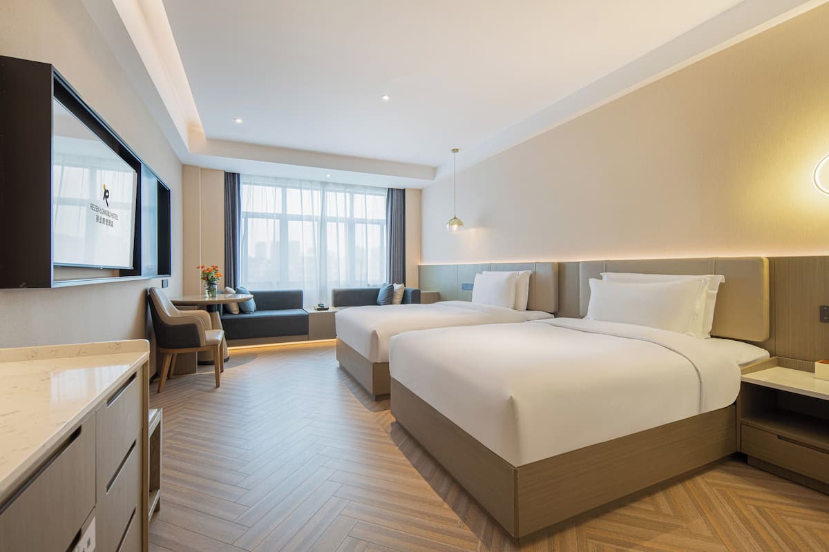 A hotel room with two beds, a desk, a sofa, and a TV.