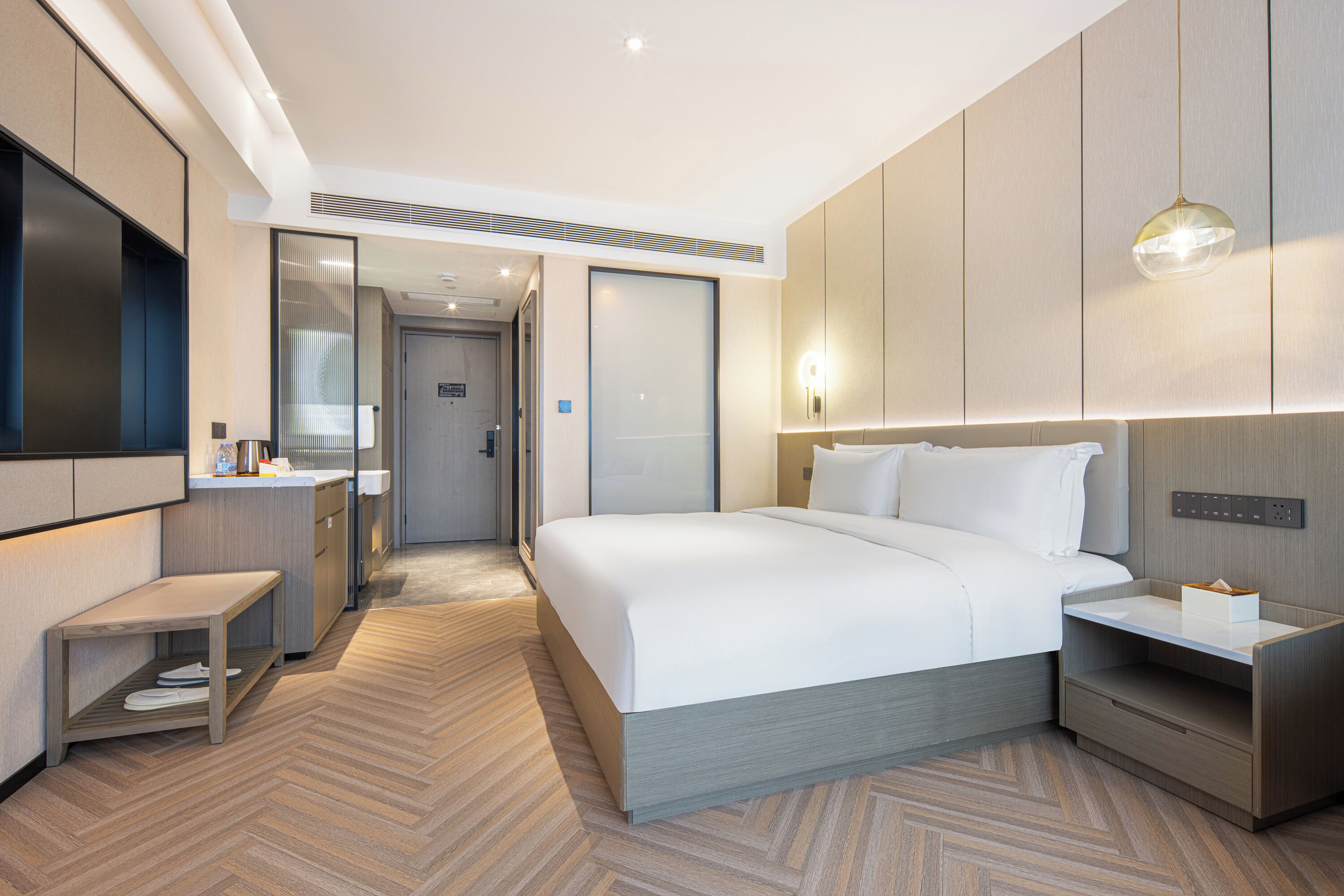 Ein modernes Hotelzimmer mit einem großen Bett, Nachttischen, einem Fernseher und einem Badezimmer mit Spiegel und Waschbecken.