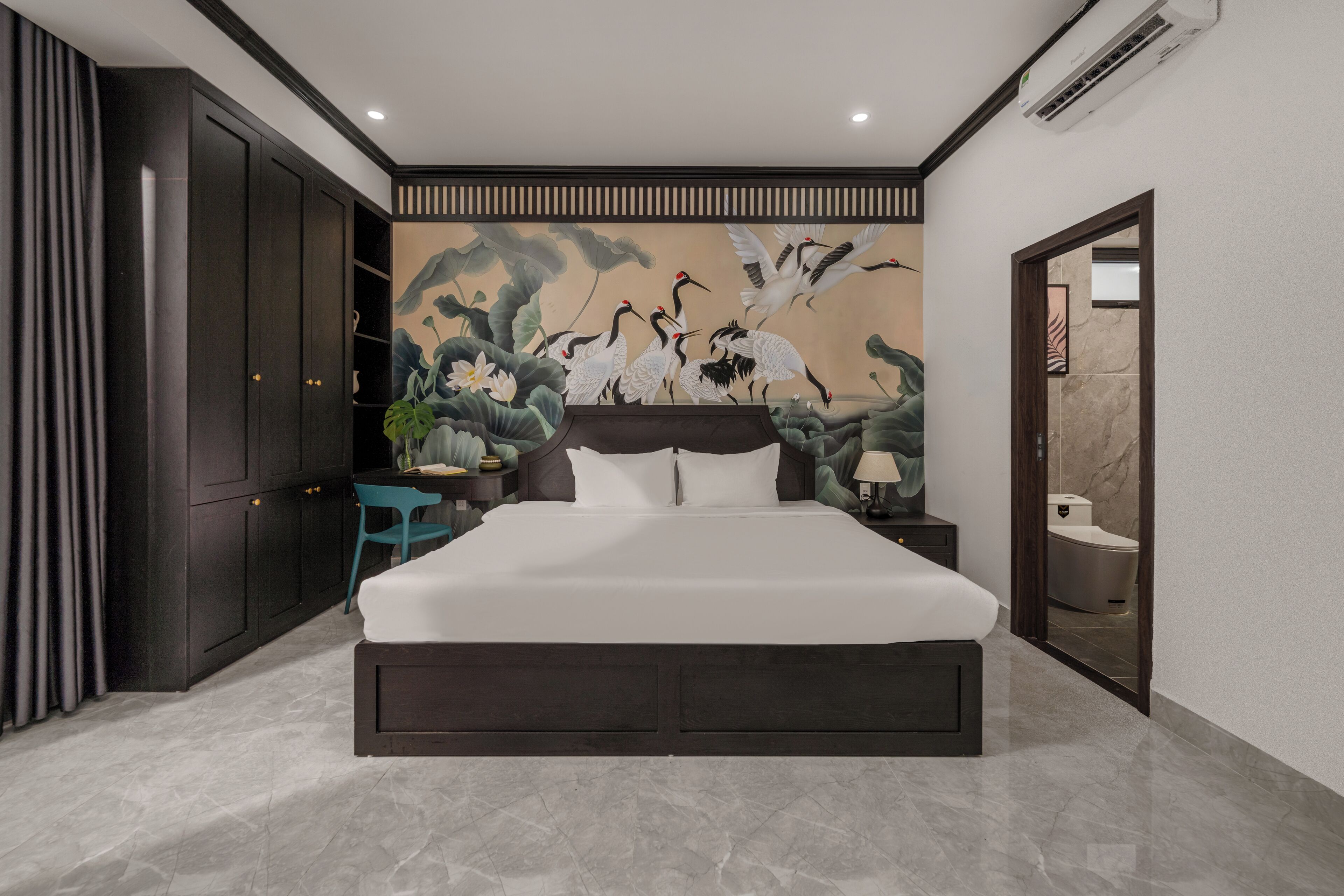 Un dormitorio moderno con una cama grande, un armario de madera oscura, un mural de grullas y un baño visible a través de una puerta abierta.