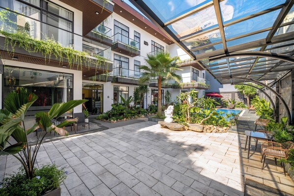 A modern building with multiple balconies, a glass ceiling, and a courtyard with plants and seating areas.