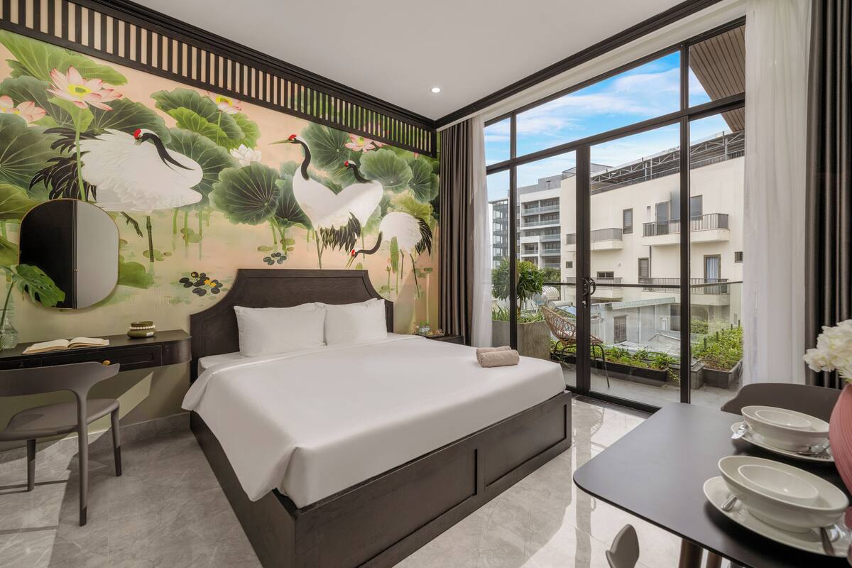 Une chambre d’hôtel moderne dotée d’un grand lit, d’un bureau avec une chaise, d’une table à manger avec des bols, et offrant une vue sur la ville grâce à de grandes fenêtres.