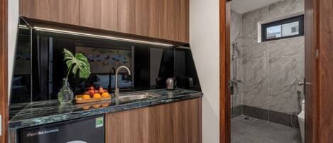 A modern kitchen with wooden cabinets, a marble countertop, and a sink. There is a small window in the adjacent bathroom.