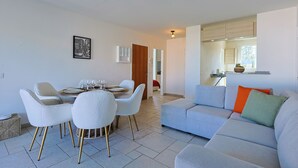 A modern living room with a dining area, a sofa, and a kitchen in the background.