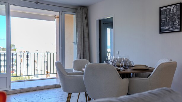A dining area with a table set for four, a sofa, and a balcony with a view.