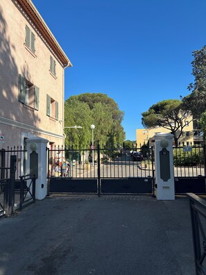 A gated entrance to a building with a clear sky, a tree, and a street in the background.
