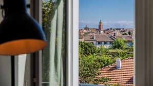 A view from a window with a lamp, overlooking a town with buildings and a tower.