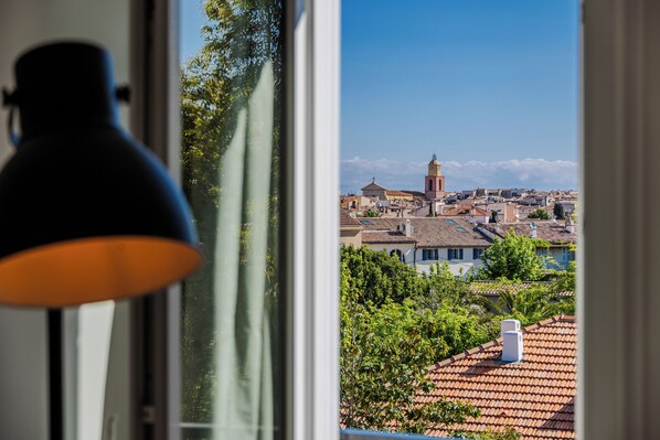 A view from a window with a lamp, overlooking a town with buildings and a tower.