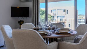 A dining area with a round table set for six, surrounded by six chairs. A flat-screen TV is mounted on the wall above the table.