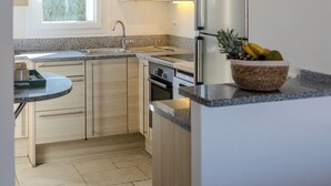 A modern kitchen with light wood cabinets, a stainless steel refrigerator, and a window providing natural light.