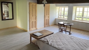 A room with a bed, a table, and two windows. - Gîte le Haut des Lariers (Morlet)