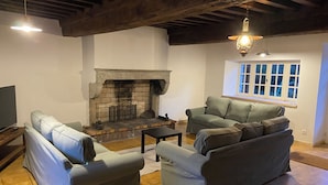 A living room with two sofas, a fireplace, and a window with white shutters. - Gîte le Haut des Lariers (Morlet)