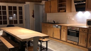 A kitchen with wooden cabinets, a dining table, and a bench. - Gîte le Haut des Lariers (Morlet)