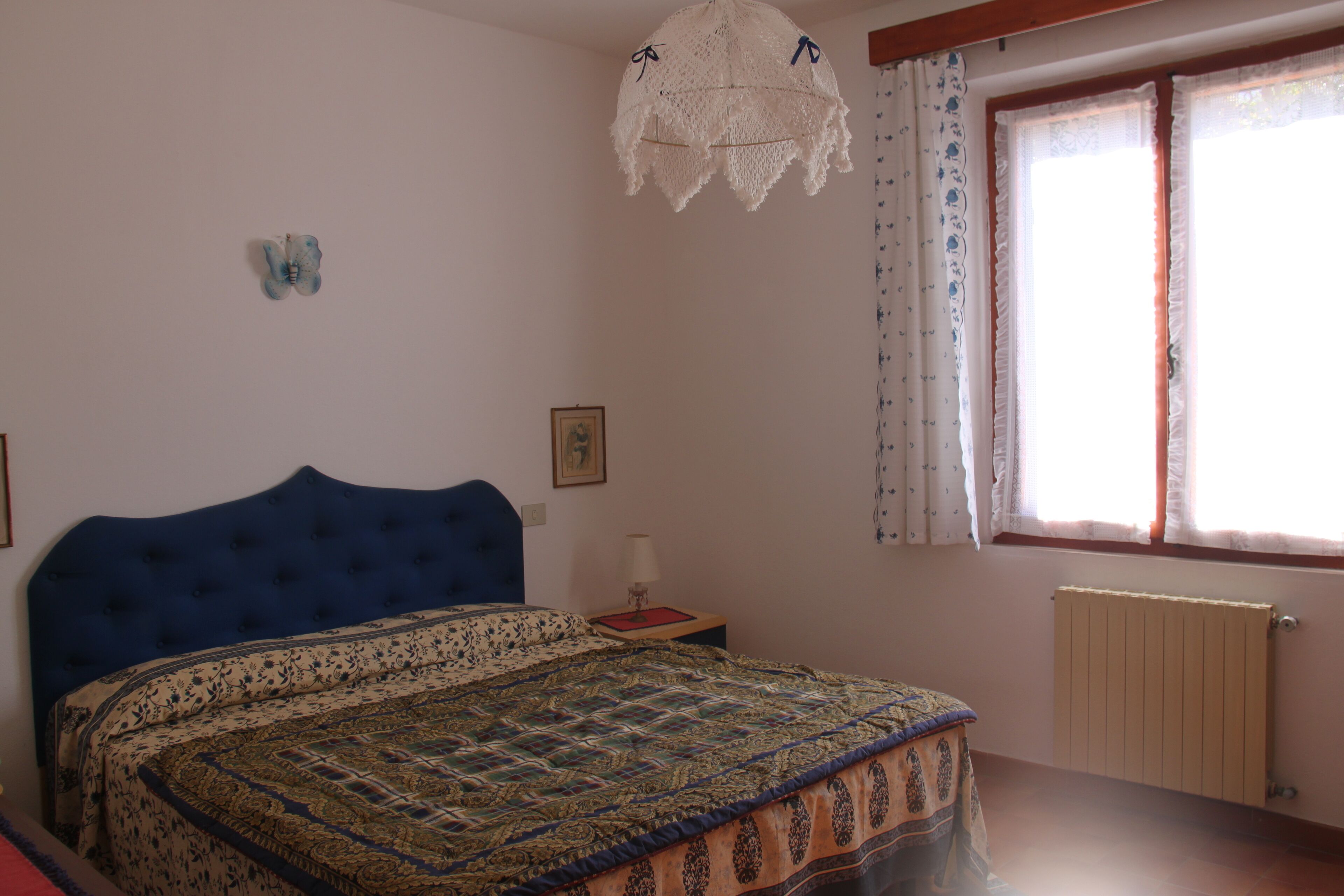 A bedroom with a large bed, a bedside table, a window with curtains, and a radiator.