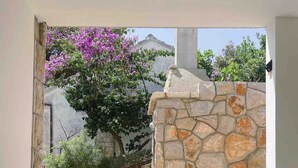 A stone-walled courtyard with a potted plant and a tree with purple flowers. - 3-Bedroom Apartment in Prizba with Ocean Views - Ideal for Families and groups (Smokvica)
