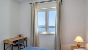 A bedroom with a bed, a desk, a chair, a lamp, and a window with curtains. - 3-Bedroom Apartment in Prizba with Ocean Views - Ideal for Families and groups (Smokvica)