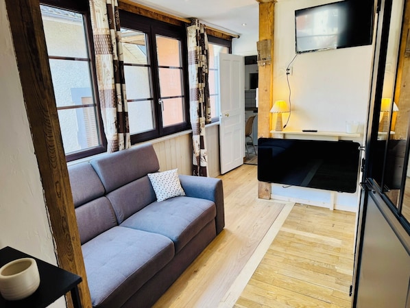 A modern living room with a sofa, a television mounted on the wall, and a wooden floor.