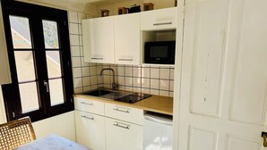 Une cuisine de taille réduite avec des meubles blancs, un micro-ondes noir et une table en bois accompagnée de chaises en osier.