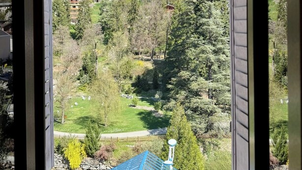 Une vue depuis une fenêtre d’un bâtiment, donnant sur un paysage montagneux avec des maisons et de la végétation.