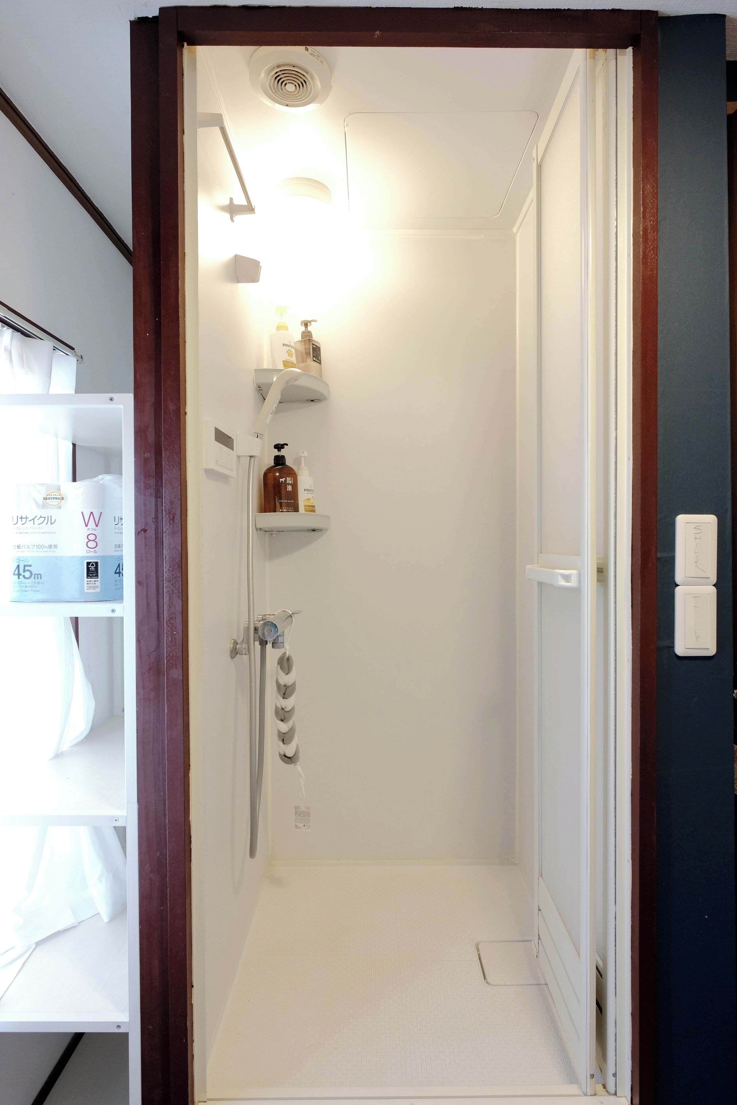 A small, well-lit bathroom with a shower, a toilet, and a shelf with toiletries.
