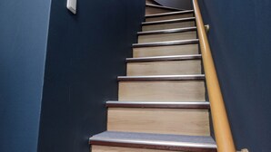 Eine Treppe mit Holzbodenstufen und einem gelben Geländer, die zu einer Zwischenebene mit einem Lichtschalter führt.