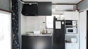 Eine kompakte Küche mit einem schwarzen Kühlschrank, einer Mikrowelle und einer Kaffeemaschine auf einem weißen Regal.