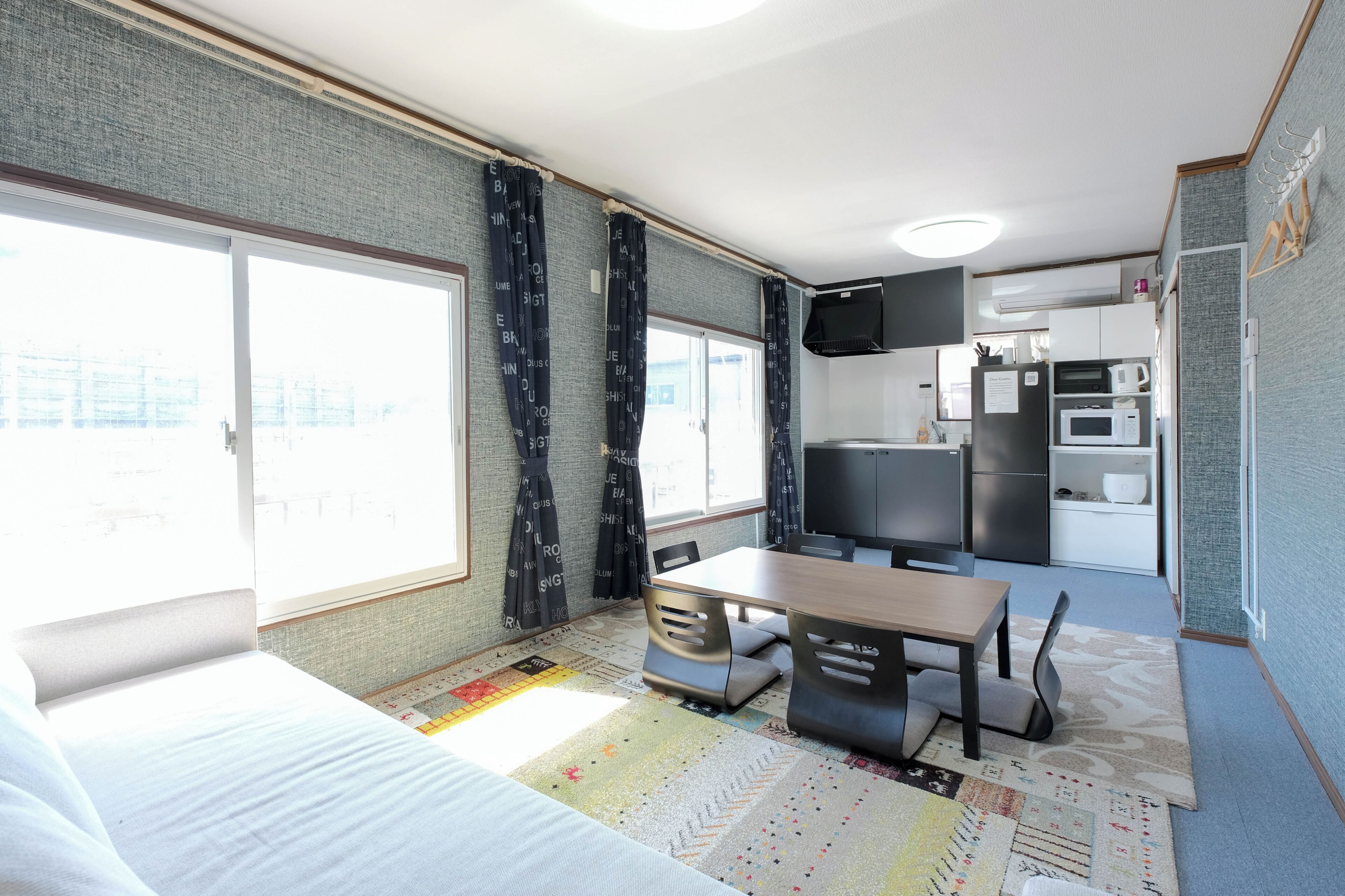 Una habitación compacta con cama, una mesita, una silla, kitchenette y televisor.