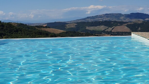 A clear blue pool with a view of rolling hills and a distant mountain range.