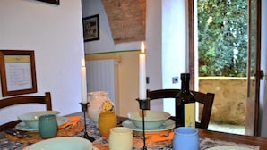 A dining table set with plates, bowls, and a candle. There are chairs around the table, and a window with a view of greenery outside.