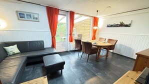 Een gezellige kamer met een bank, een eettafel met stoelen, en een houten bankje.