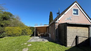 Een houten huis met een overdekte veranda, een garage en een tuin met een haag en gazon.