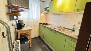 Een kleine keuken met groene kastjes, een roestvrijstalen spoelbak en een koffiezetapparaat.