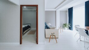 A modern hotel room with a large bed, a sitting area with a coffee table, and a dining area with a table and chairs.