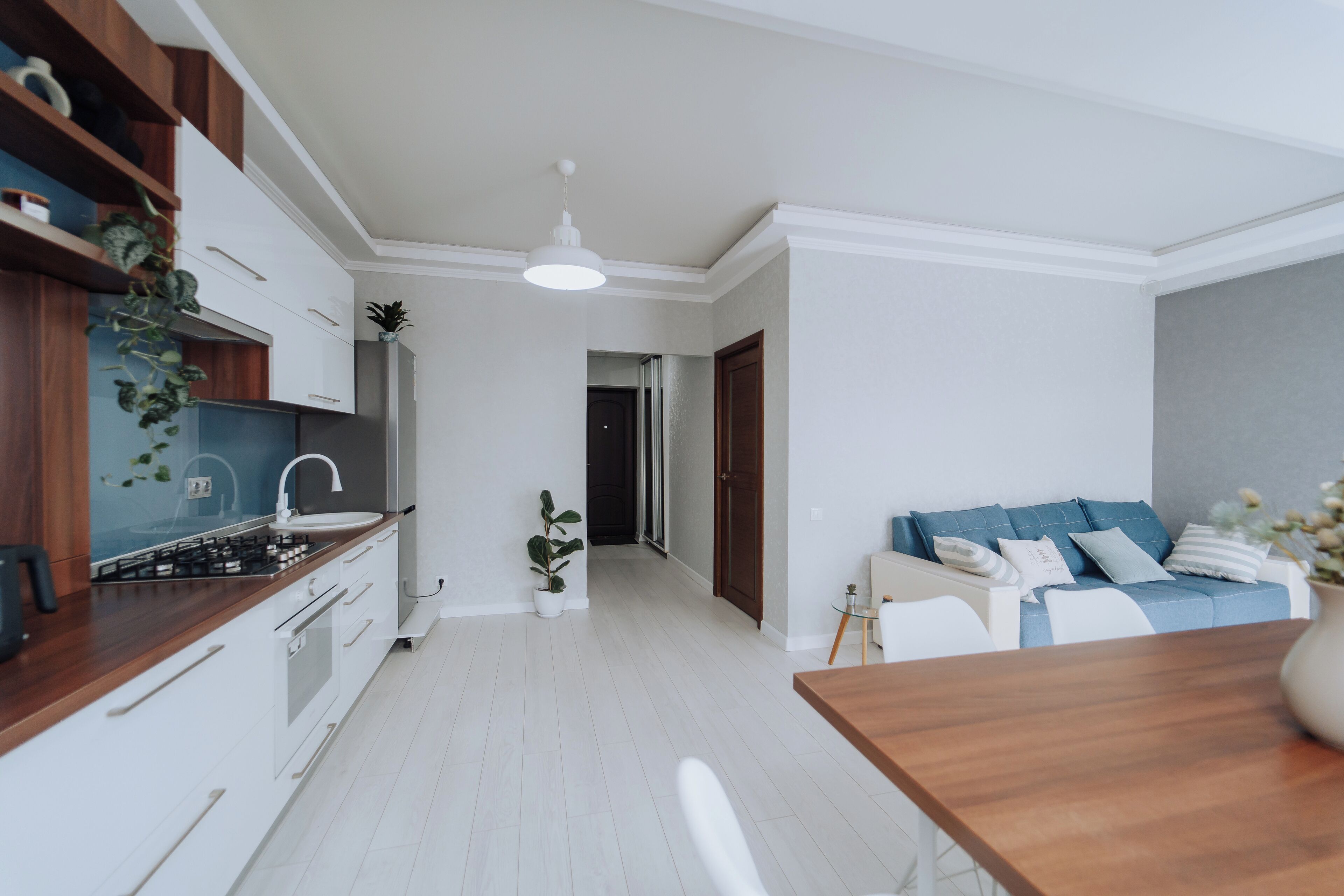 A modern kitchen with white cabinets, a wooden countertop, and a built-in stove. There is a dining area with a wooden table and chairs, and a blue sofa with cushions.