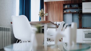 A modern kitchen with white cabinets, a wooden countertop, and a dining area with a glass table and white chairs.