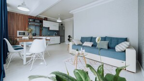 A modern living room with a blue sofa, white chairs, and a glass coffee table.
