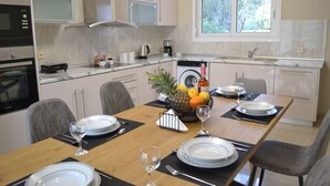 A modern kitchen with a dining area. It includes a microwave, oven, sink, and a window with a view of trees.