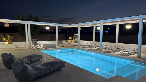 A modern outdoor pool area with lounge chairs and bean bags, surrounded by a covered patio with large windows.