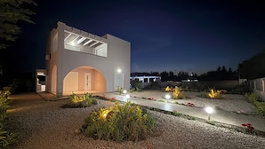 A modern building with a unique architectural design, featuring a large arched entrance and a well-lit garden area with gravel pathways and plants.
